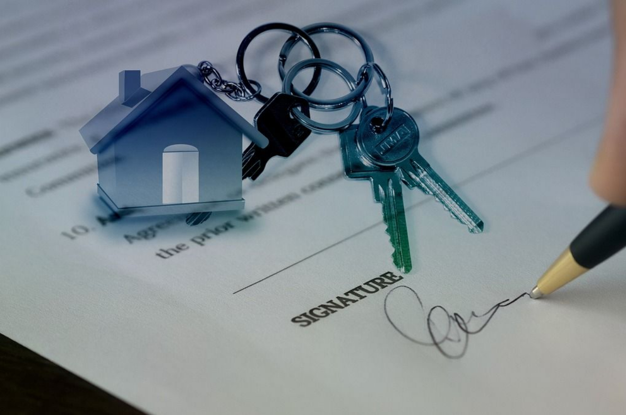 Close-up of a house purchase contract being signed, with house keys and a small house model, symbolizing successful homeownership.