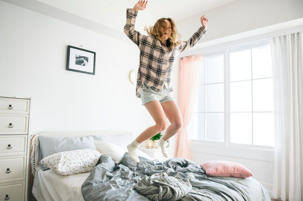 Joyful woman jumping on the bed in her new UK home, celebrating a successful mortgage deal.